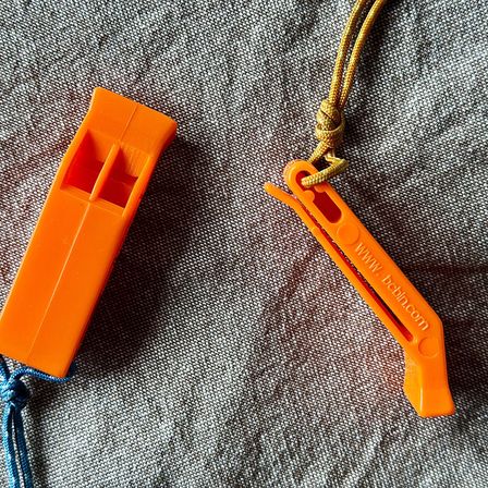 Two bright orange plastic whistles on a canvas surface