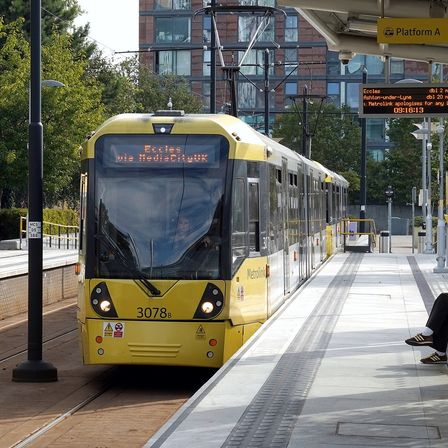 A yellow Metrolink tram at a platform, one passenger waiting