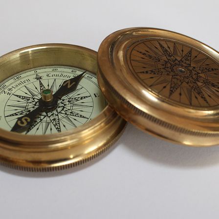 An open brass pocket compass on a white surface